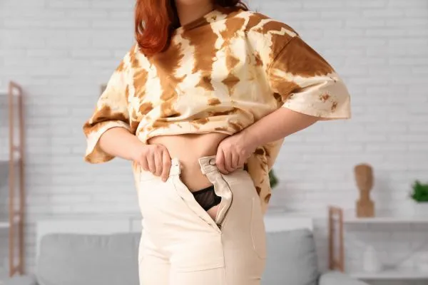Image of woman trying to do her trousers up after pregnancy weight gain Dumbarton