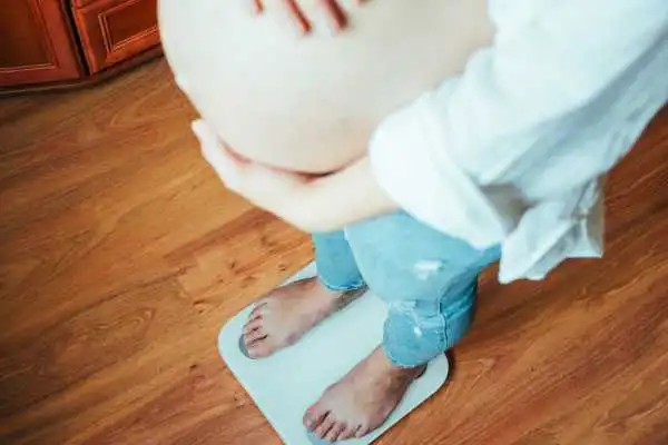 Image of woman weighing herself and experiencing weight gain through pregnancy Dumbarton